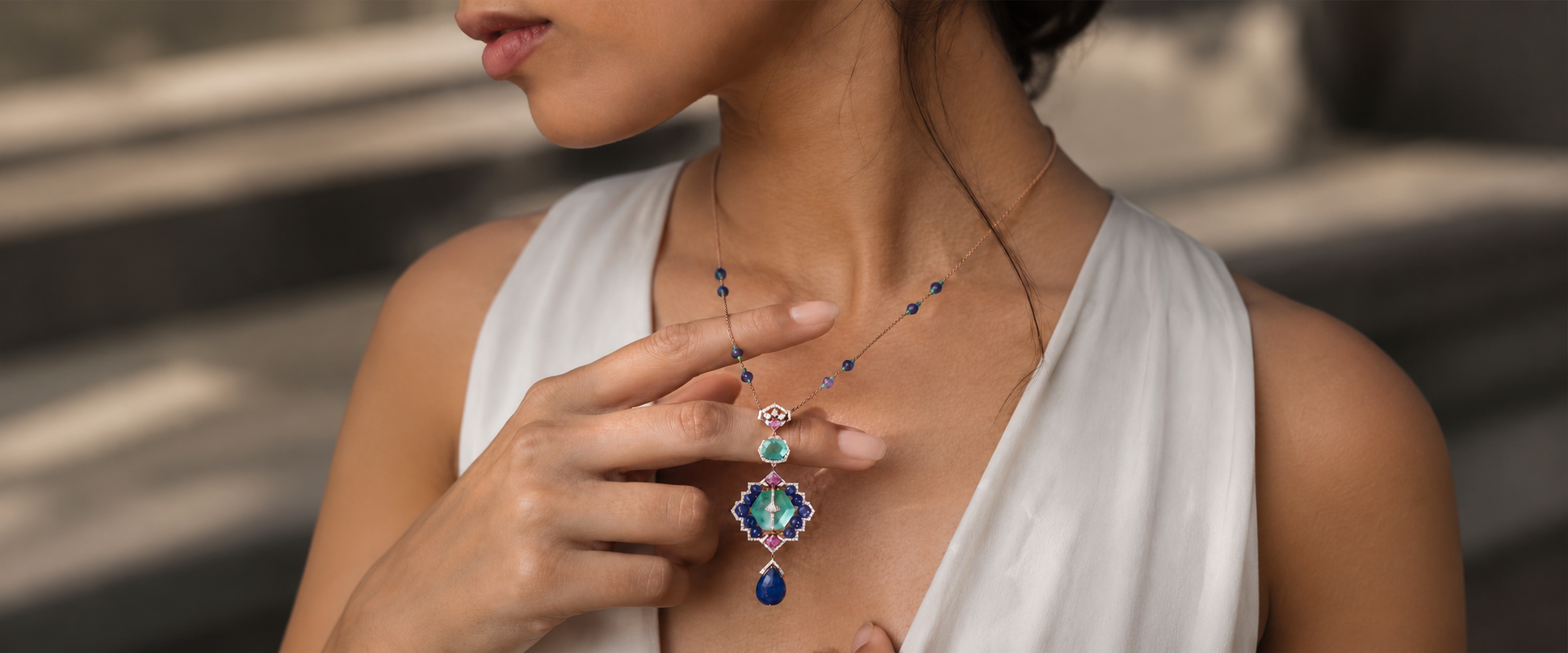 An emerald and sapphire pendant worn on a rose-gold chain